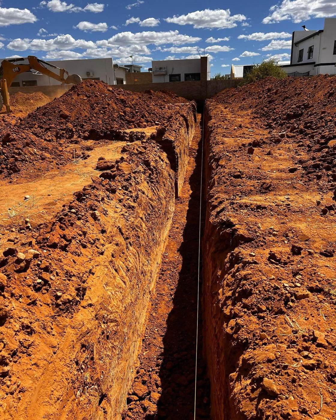 Deep service trench cut through red Namibian earth on an Africardo civils site